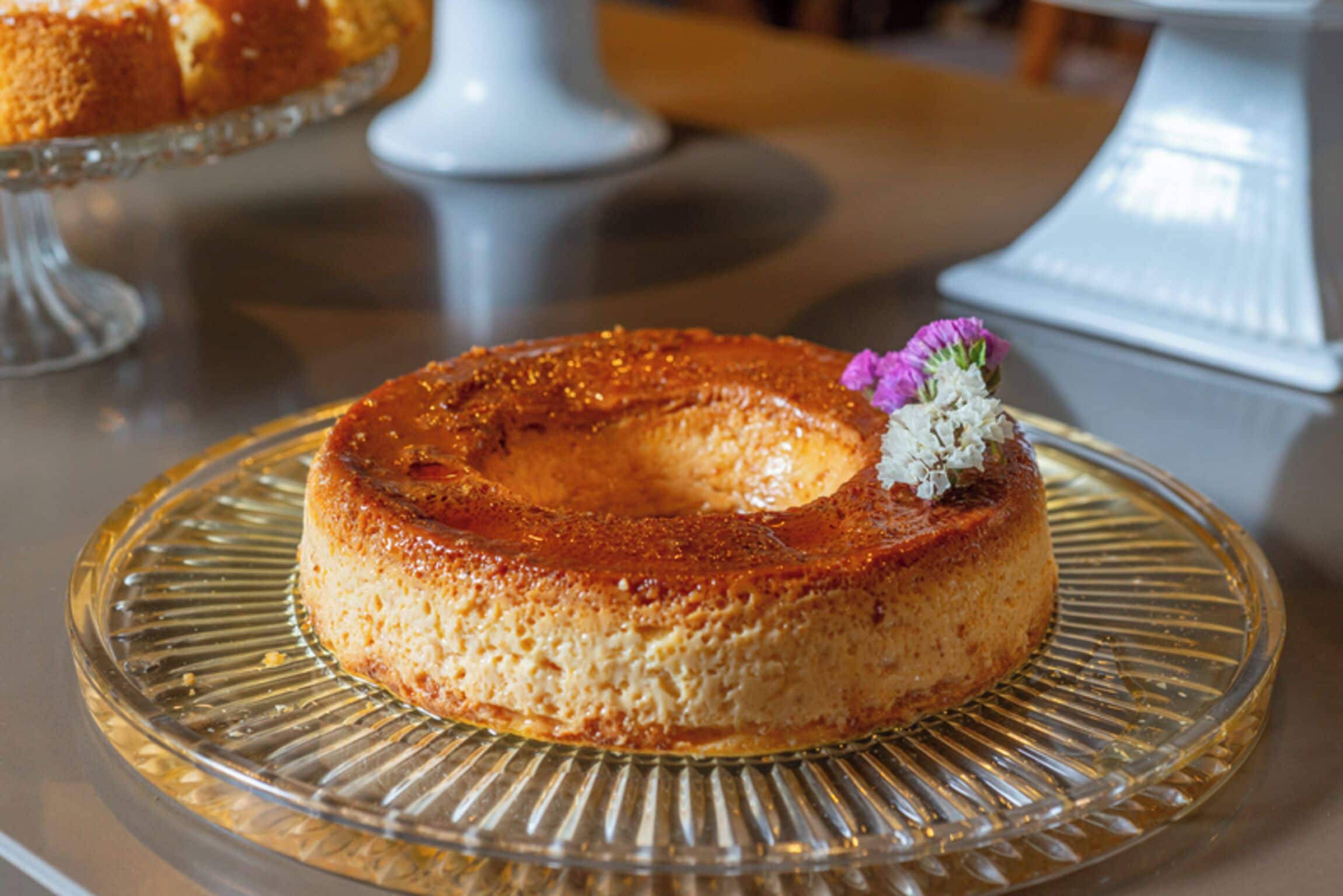 A round cake on a clear glass plate with a decorative flower on top.