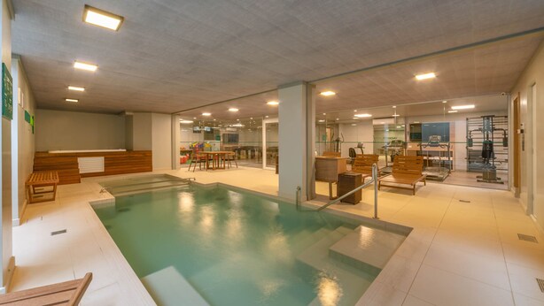 An indoor swimming pool with benches, a changing room, and exercise equipment. - Hotel Laghetto Fratello (Gramado)