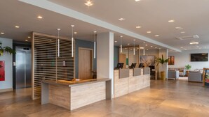 A modern reception area with a wooden reception desk, a waiting area with chairs, and a large painting on the wall. - Hotel Laghetto Fratello (Gramado)