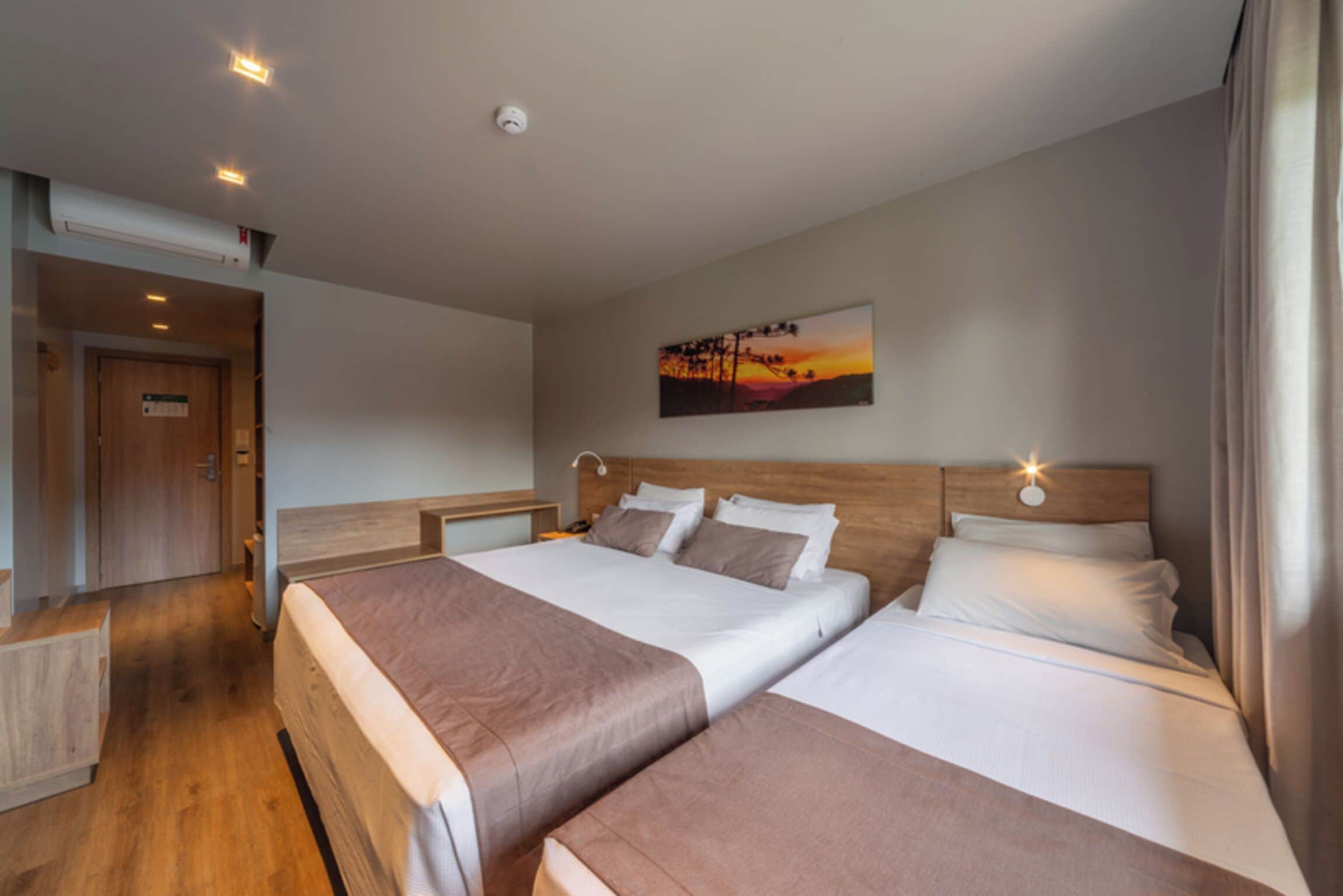 A hotel room with two beds, a wooden headboard, a painting on the wall, and a ceiling light.