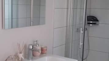 Ett modernt badrum med ett vitt handfat, en duschkabin i glas och en stor spegel ovanför handfatet.
