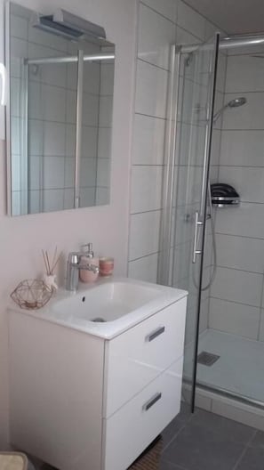 Une salle de bain moderne avec un meuble-lavabo blanc, une cabine de douche en verre et un grand miroir au-dessus du lavabo.