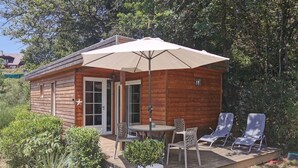 Una cabaña de madera con un balcón, una mesa y dos sillones de descanso.