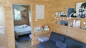 Una cabaña acogedora de madera con una cama, un sofá azul, un escritorio con una computadora e ilustraciones de pájaros en la pared.