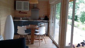 Una cocina moderna con paredes de madera, un comedor con mesa y sillas de madera, y un amplio ventanal que ofrece vistas al exterior.