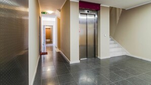 Un couloir avec un sol carrelé, un ascenseur et un escalier.