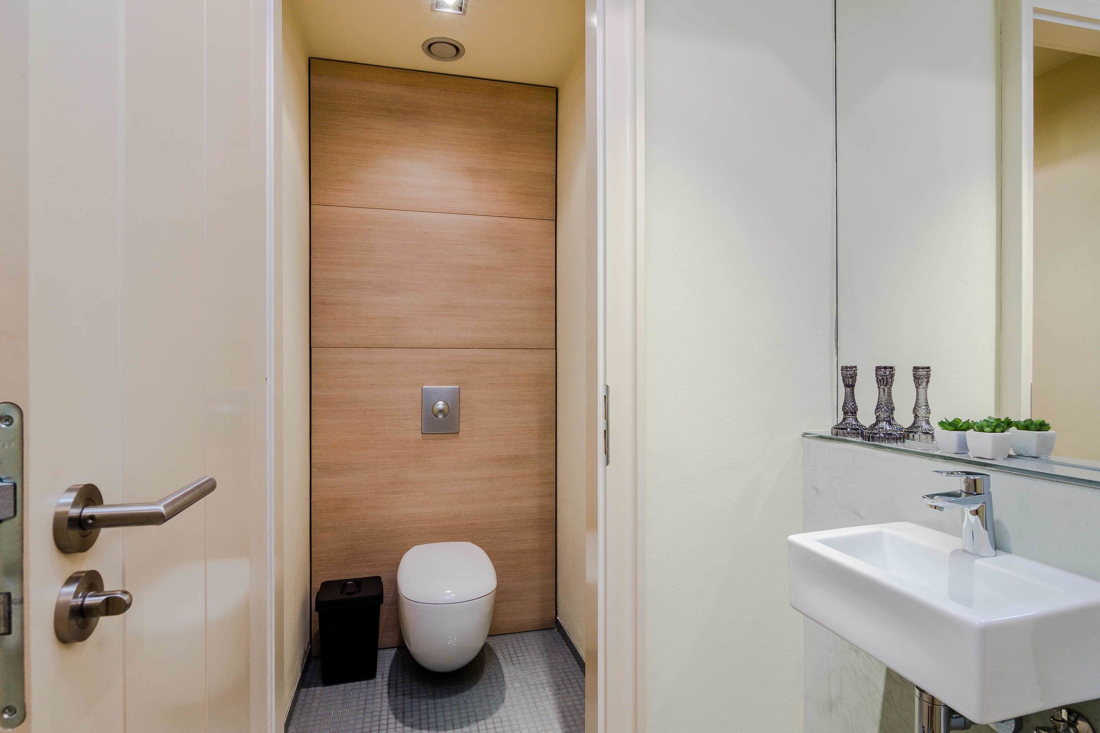 Une salle de bain moderne avec un mur en bois, des toilettes blanches, un lavabo avec un miroir et une petite plante posée sur le comptoir.