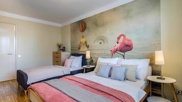 A hotel room with two beds, a mural of a flamingo and an eye, and a small round table with a lamp.