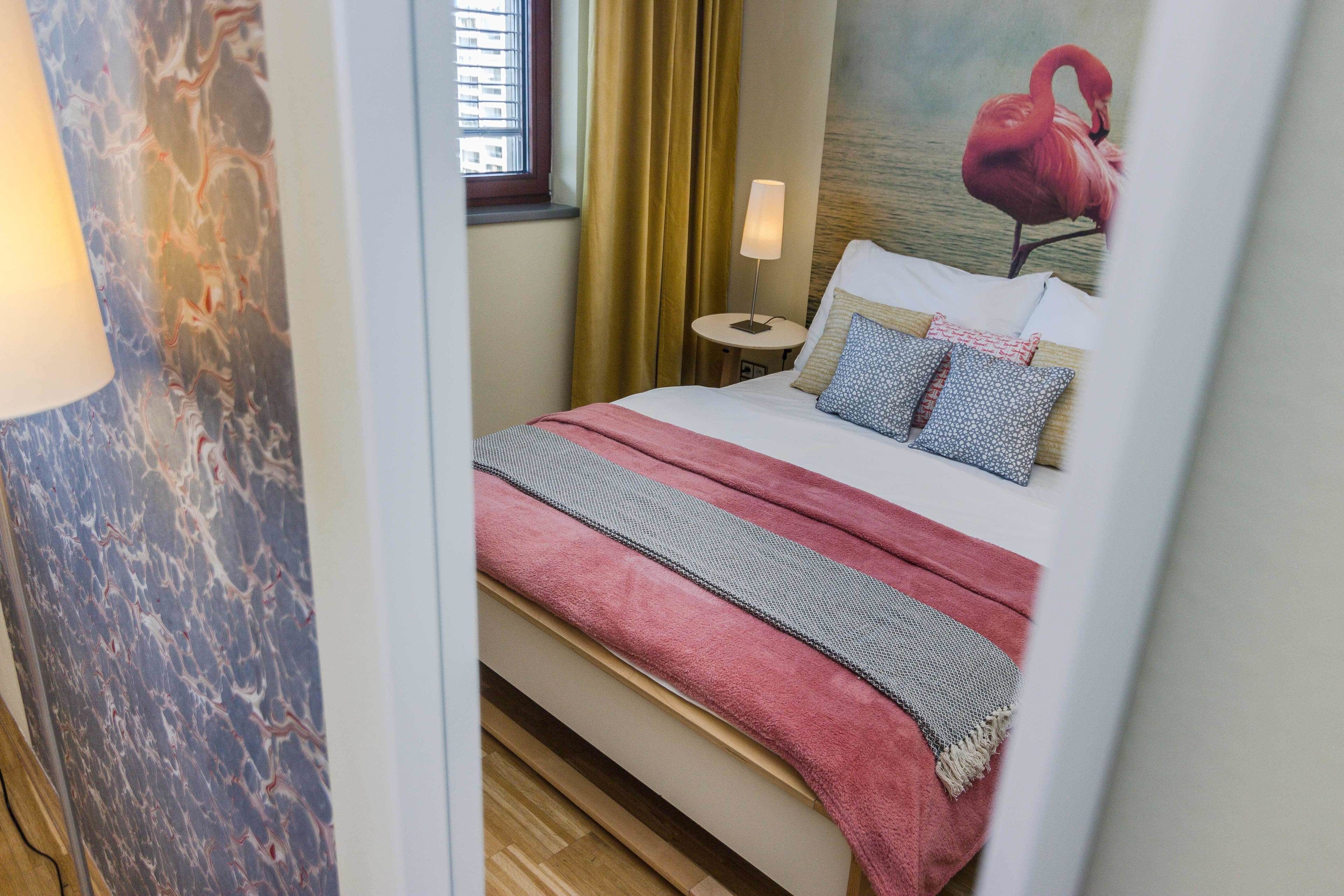 Una habitación de hotel con una cama, una mesita de noche, una lámpara y una ventana con cortinas.
