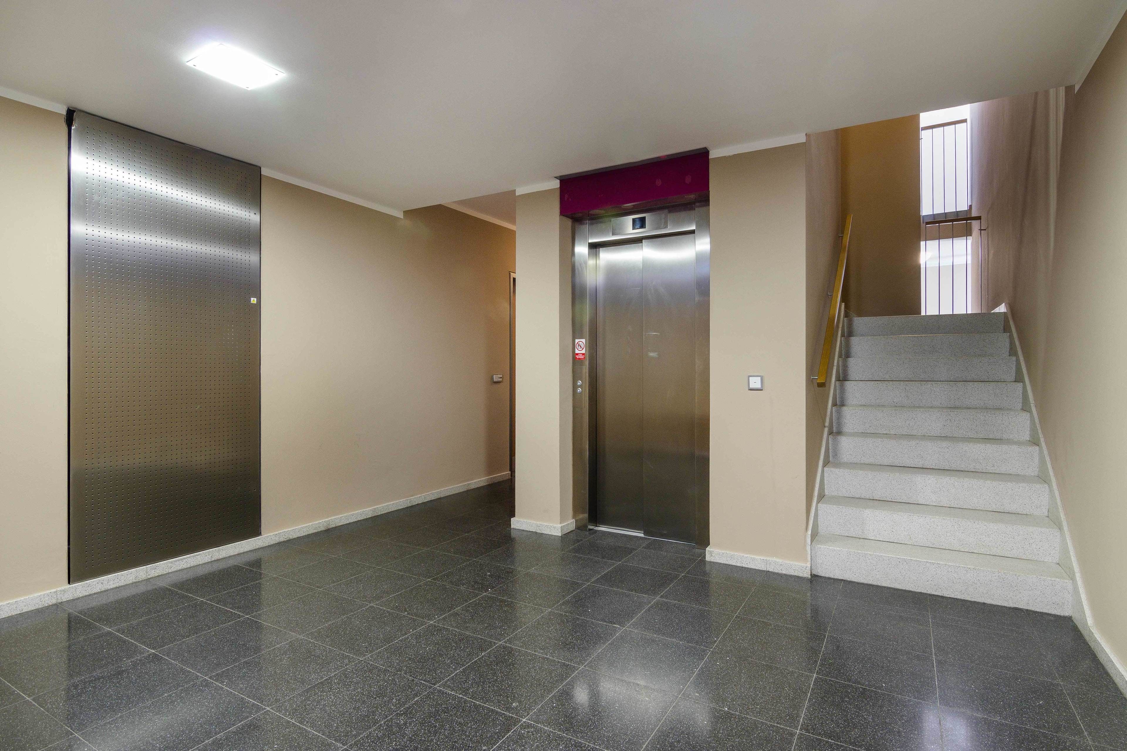 Un pasillo con piso de baldosas, un ascensor y una escalera.