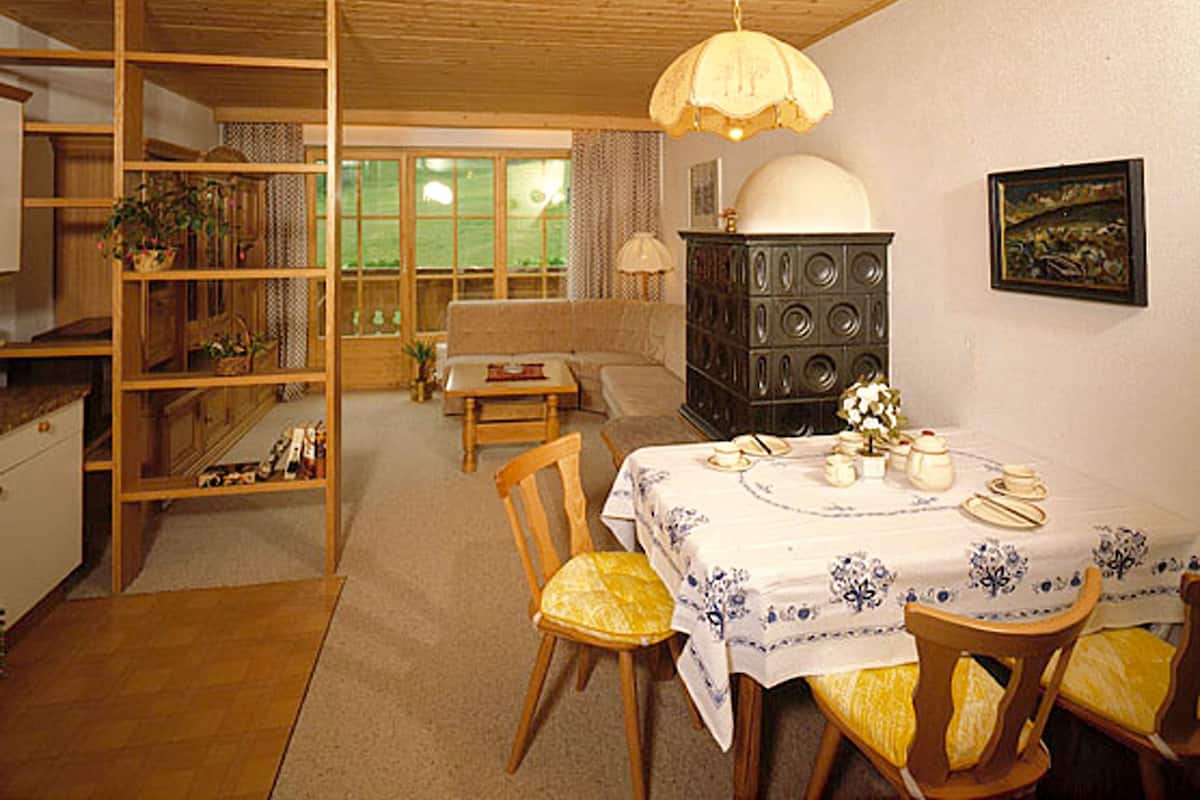 Un salon chaleureux avec une table à manger pour deux, une bibliothèque et une grande fenêtre donnant sur un paysage verdoyant.