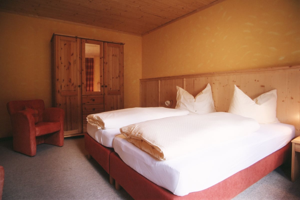 Une chambre avec deux lits, une armoire en bois et une chaise rouge.