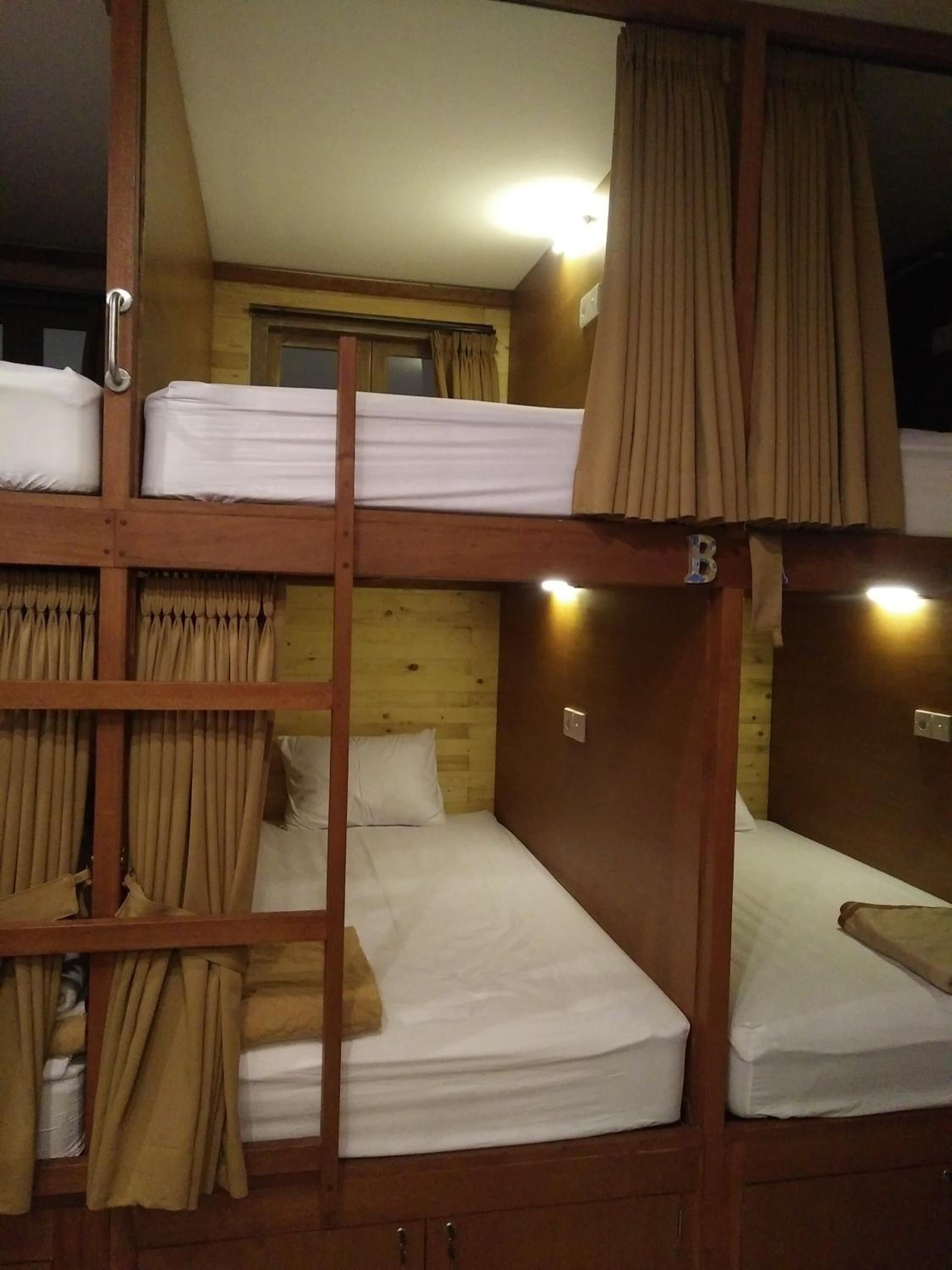 Une chambre avec des lits superposés, des murs en bois et une fenêtre. Il y a des rideaux à la fenêtre et une échelle qui mène au lit supérieur.