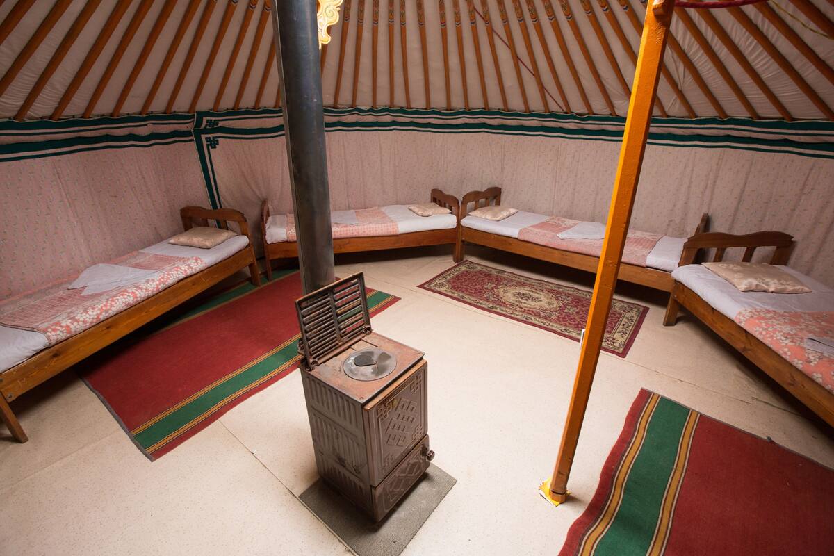 L’intérieur d’une yourte traditionnelle, avec trois lits en bois, un poêle à bois servant de chauffage central et des tapis aux couleurs vives.