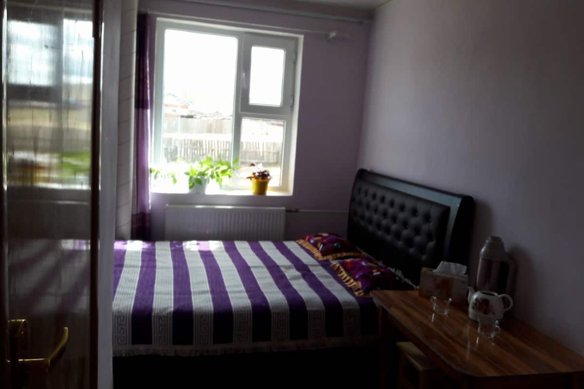 Une chambre à coucher avec un lit, une fenêtre donnant sur un beau paysage, un radiateur et une table de chevet sur laquelle se trouvent une tasse et une soucoupe.