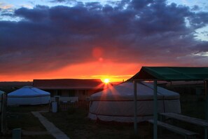 Uma yurta com telhado verde, uma tenda branca e um banco de madeira num camping.
