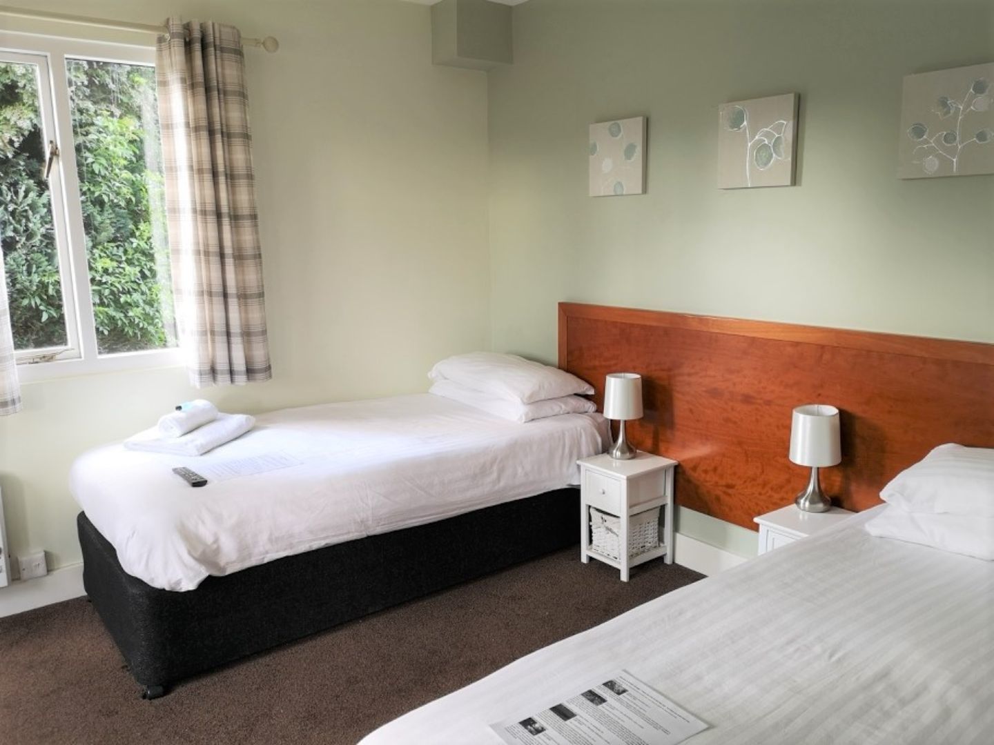 A hotel room with two beds, a window with curtains, a wooden headboard, and wall art.