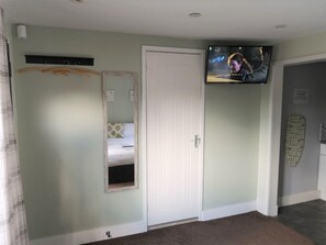 A bedroom with a bed, a mirror, a television mounted on the wall, and a door. - Swedish Cottages (Luton)