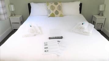 A neatly made bed with white linens, two pillows, a remote control, and a set of papers on the bed.