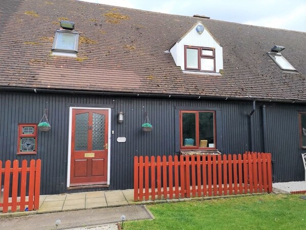 A two-story house with a red picket fence, a brown door, and a small window with a white frame. - Swedish Cottages (Luton)