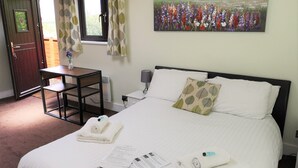 Een hotelkamer met een bed, bureau, stoel, raam met gordijnen, een schilderij aan de muur en een deur.