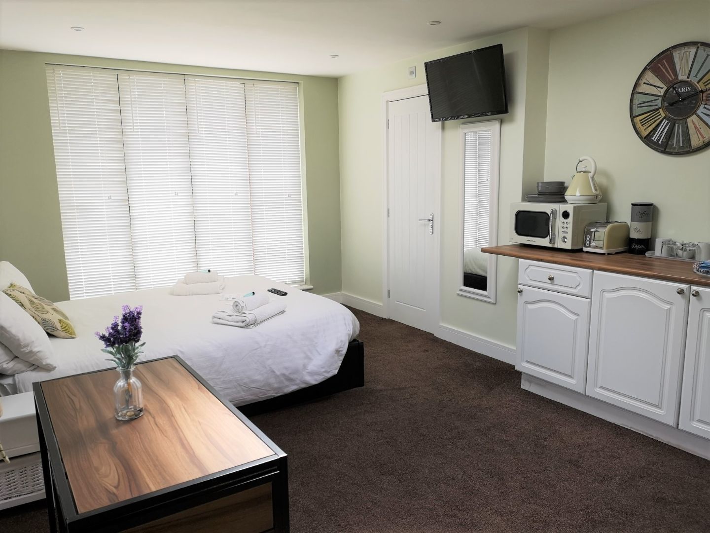 A hotel room with a bed, bedside table, TV, and kitchenette.