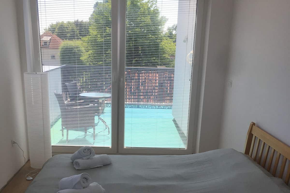 Een slaapkamer met een bed, een raam met zonwering en uitzicht op een buitenruimte.