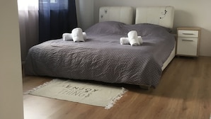 Een slaapkamer met een bed, nachtkastje, raam met gordijnen en vloerkleed.