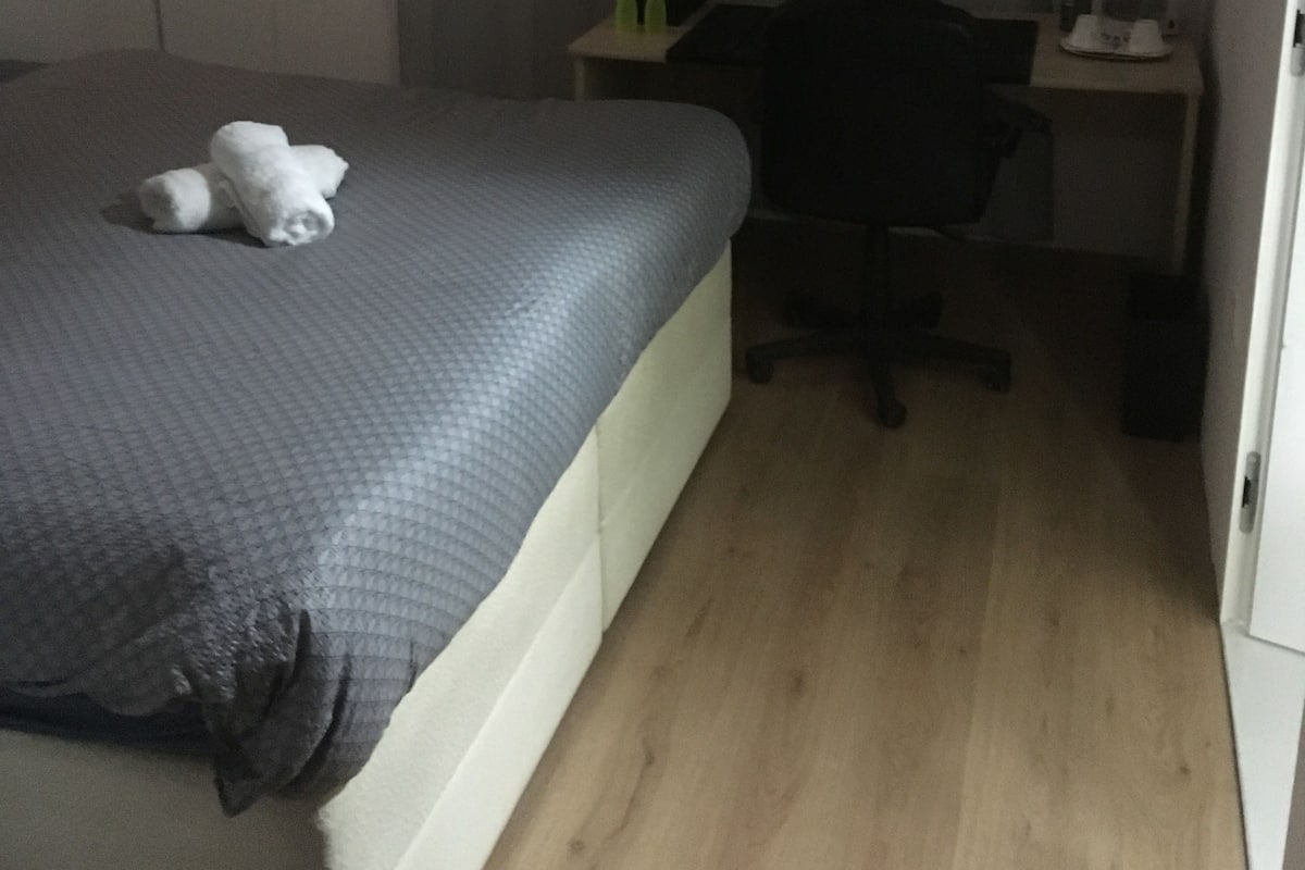 Een slaapkamer met een bed, een bureau, een stoel en een raam met gordijnen.