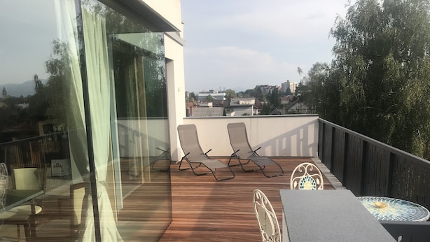 Een houten terras met twee loungestoelen en een tafel, met uitzicht op een stadsbeeld.