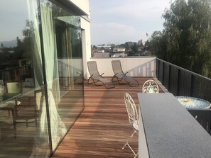 A wooden deck with two lounge chairs and a table, overlooking a cityscape. - Residence Eu Me Amo (Ljubljana)
