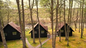 Three cabins in a forest with a gravel path leading to them. - Burnbank Lodges (Spean Bridge)