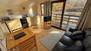 A cozy living room with a sofa and a dining table, a kitchen with a stove and sink, and a TV on a stand. - Burnbank Lodges (Spean Bridge)
