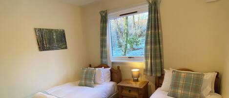 A twin room with two single beds, a bedside table with a lamp, a window with curtains, and a painting on the wall.