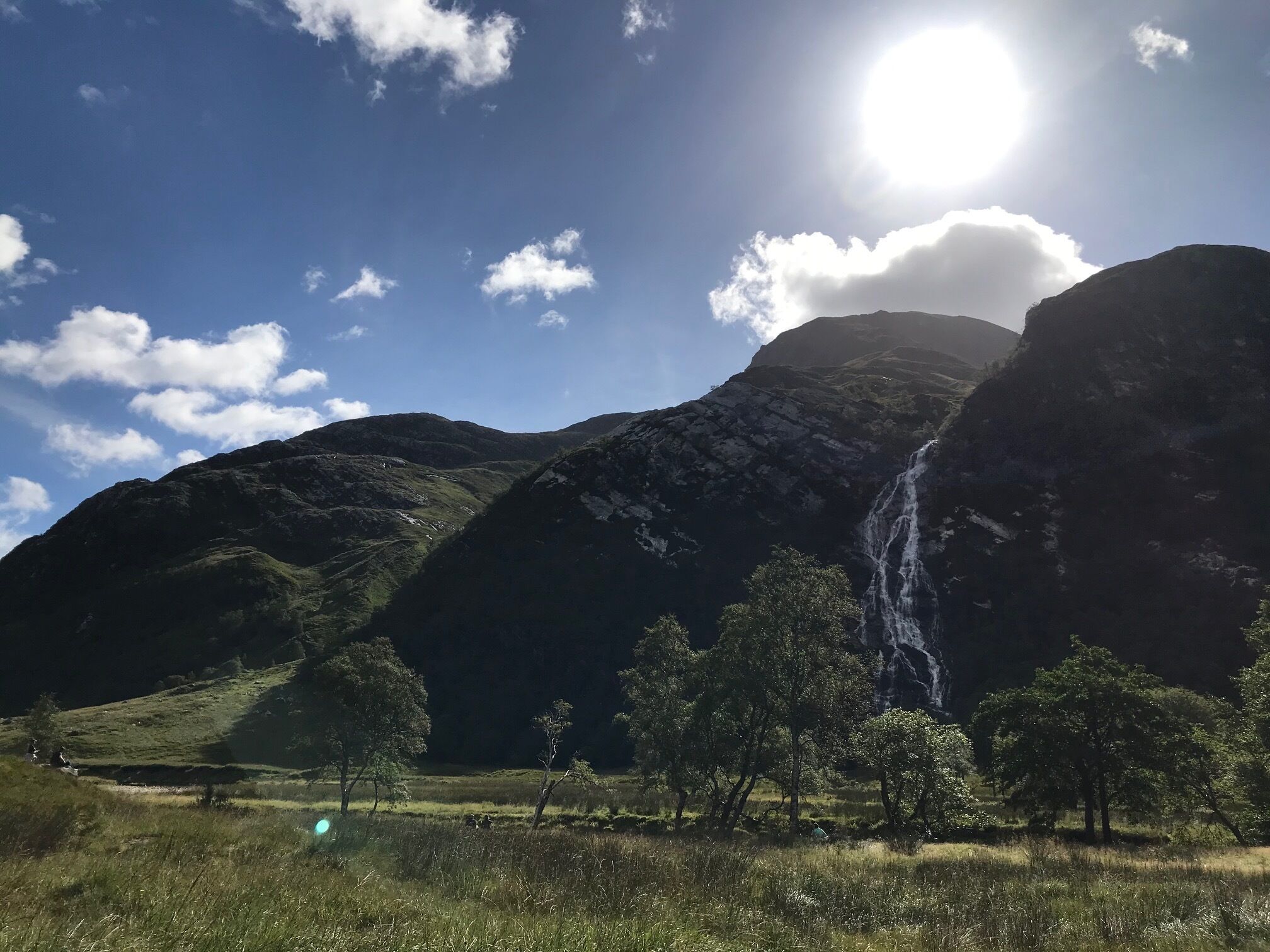 A mountainous landscape with a waterfall, trees, and a clear sky.