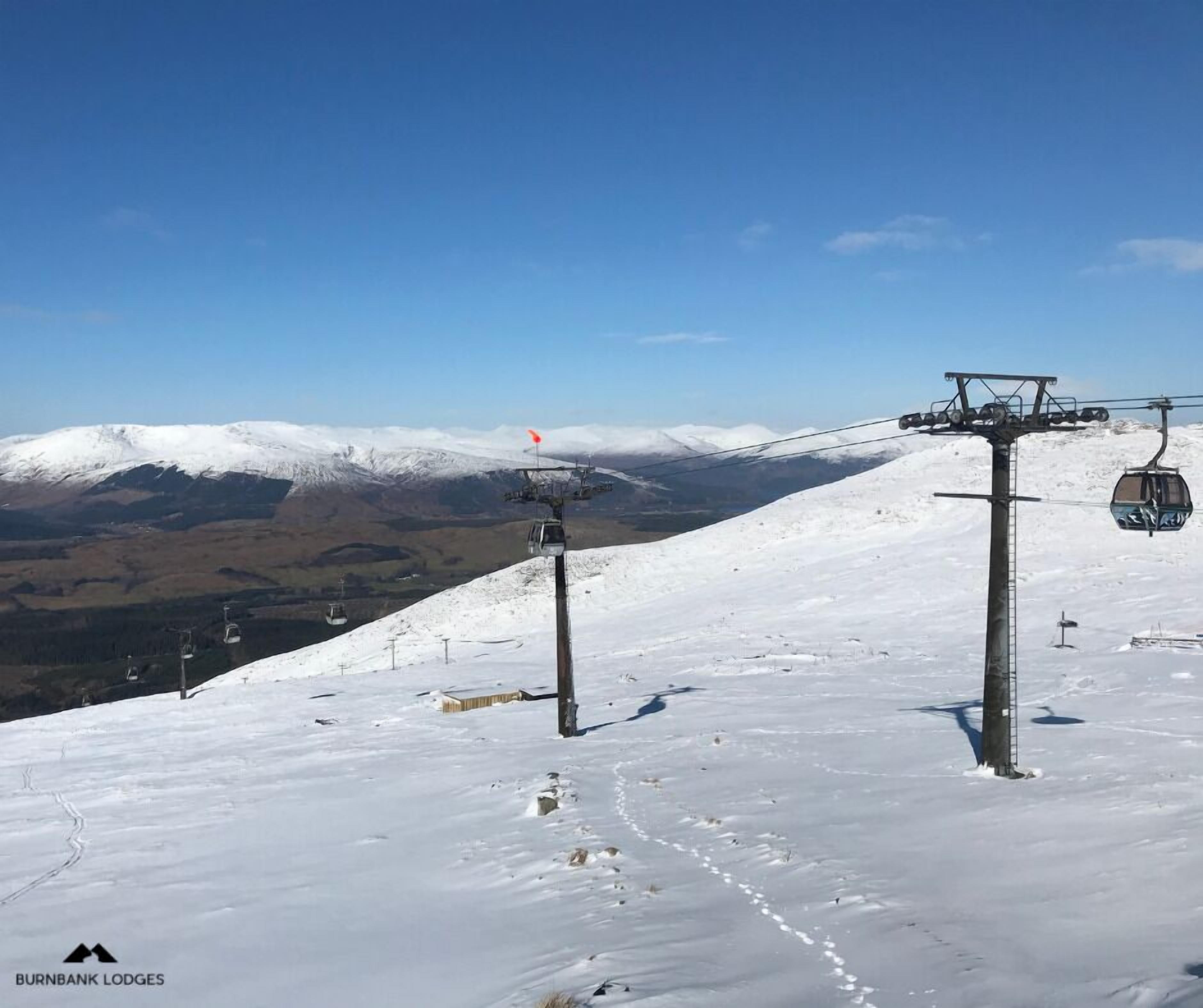 A snow-covered ski slope with ski lifts and a mountain in the background.