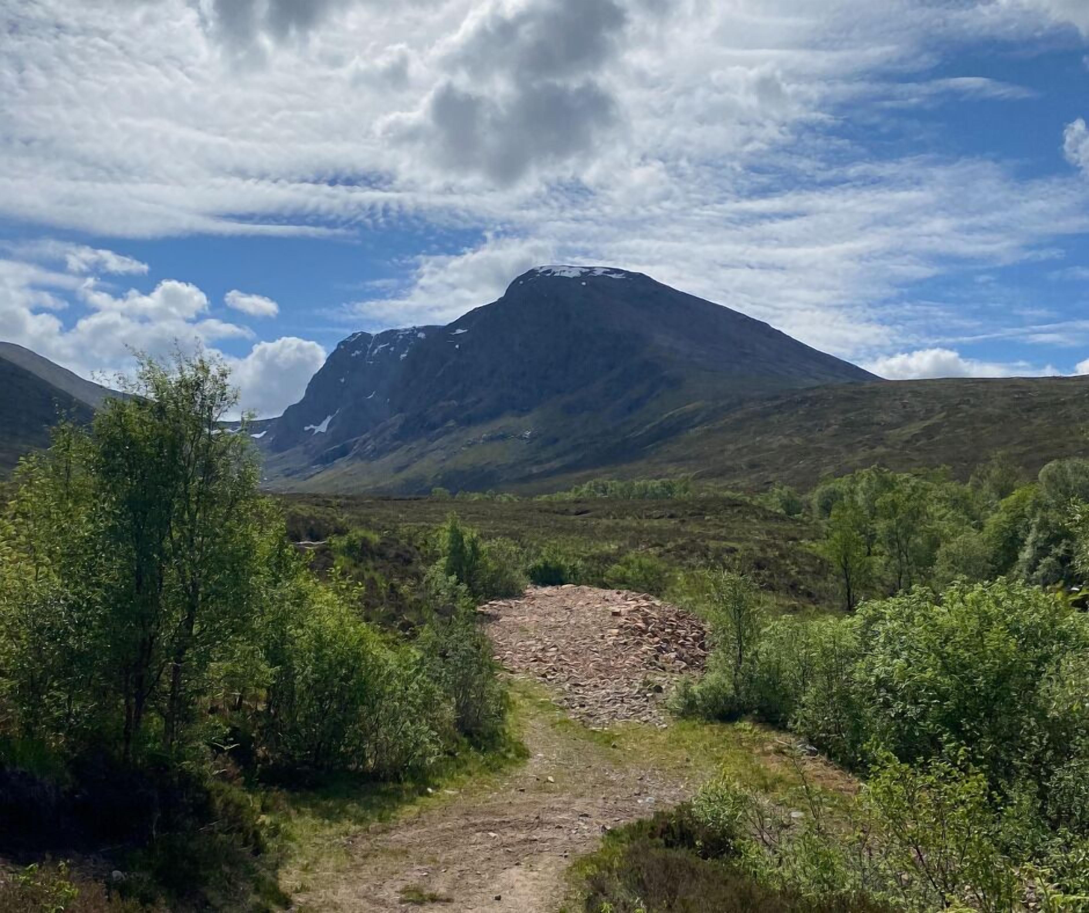 Un paysage montagneux, avec un ciel dégagé et un sentier rocailleux qui mène au sommet d’une montagne.