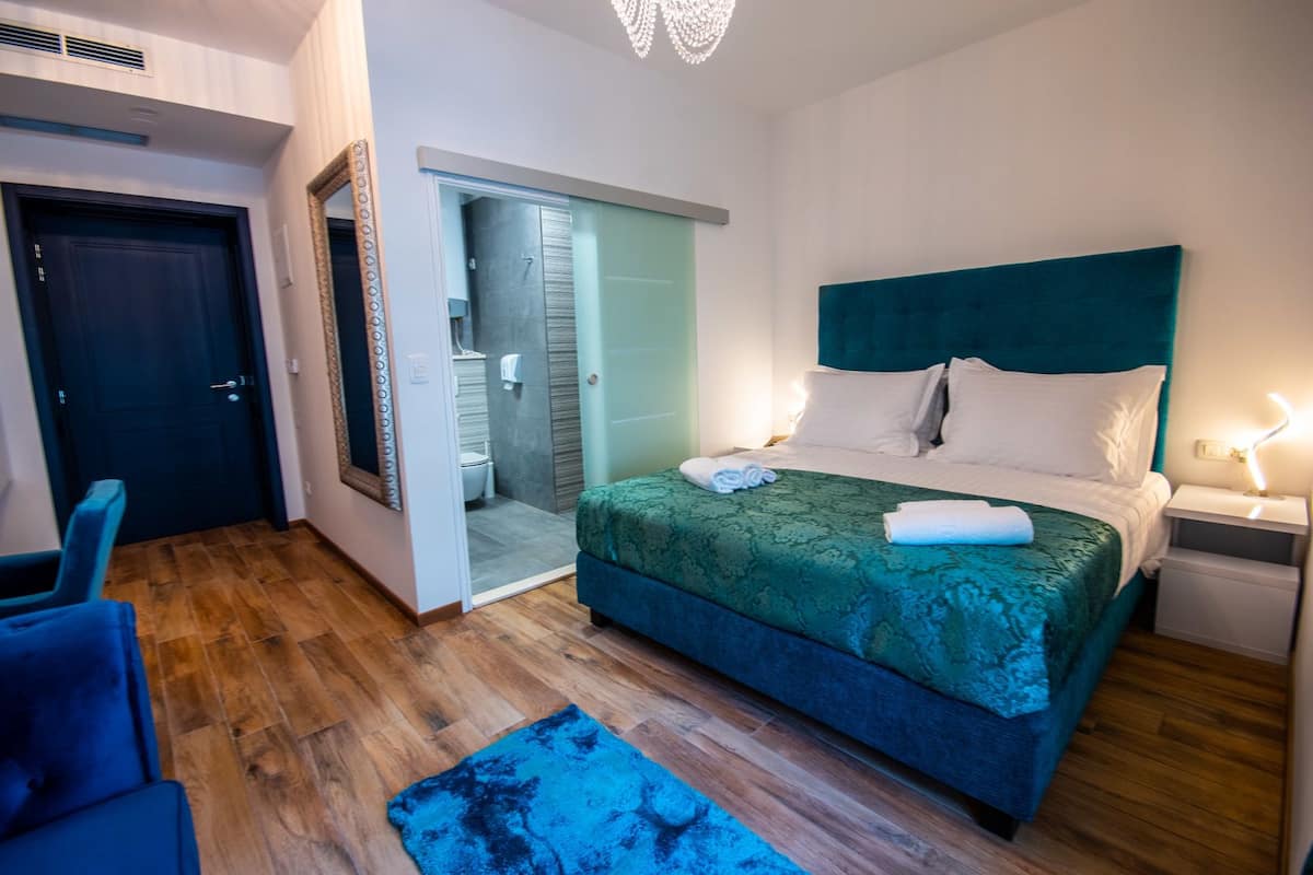 A hotel room with a bed, a nightstand, a chair, and a bathroom visible through an open door.