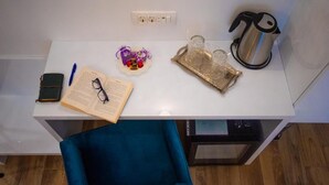 Un bureau blanc sur lequel se trouvent un livre, des lunettes, un stylo, un objet décoratif en forme de cœur, un plateau avec des verres et une bouilloire.