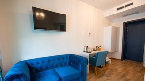 Une pièce avec un canapé bleu, un petit bureau avec une chaise, un téléviseur fixé au mur et une porte.