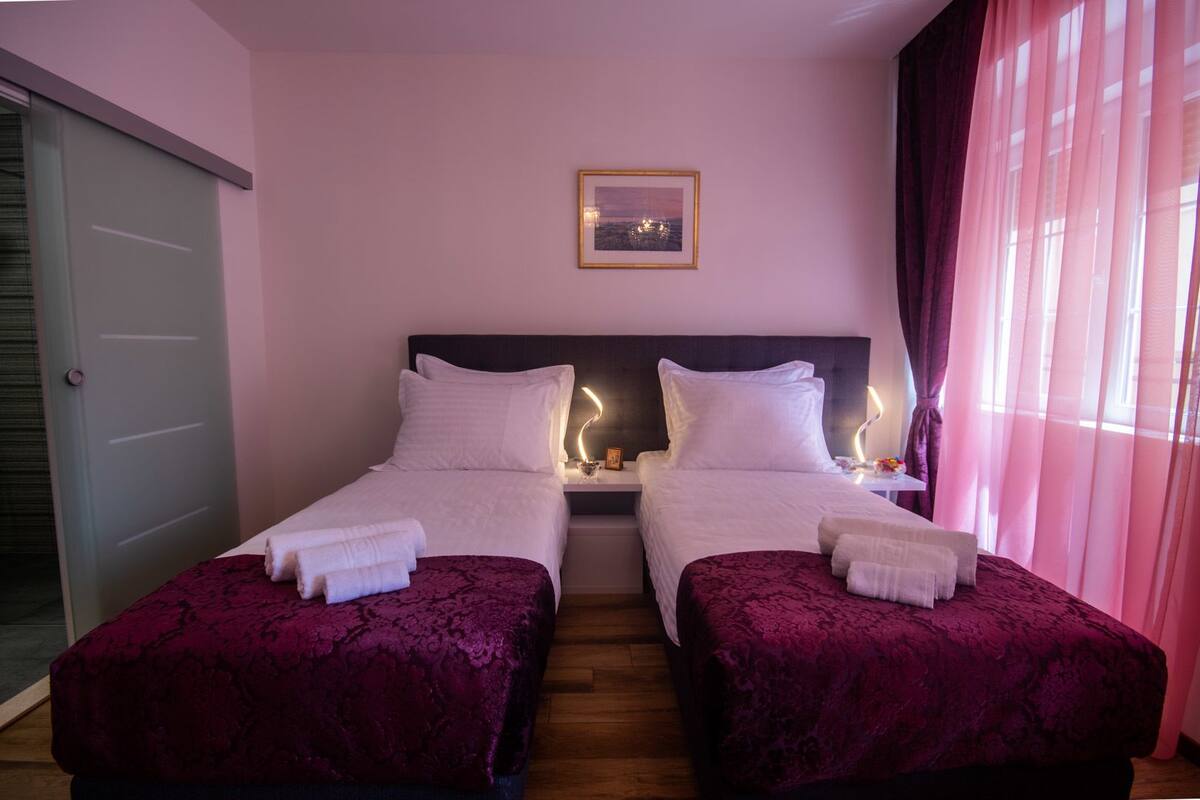 A double room with two beds, each with a headboard, a bedside table, and a lamp.