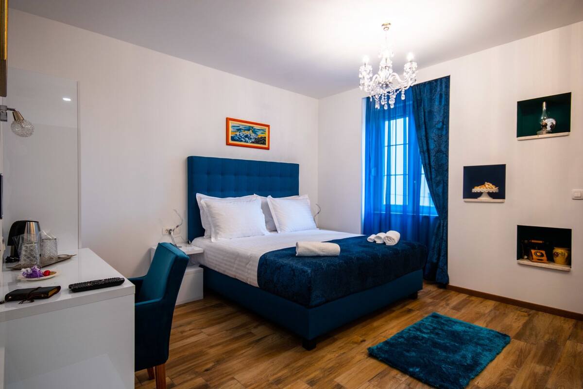 A modern hotel room with a large bed, a desk, and a chandelier.