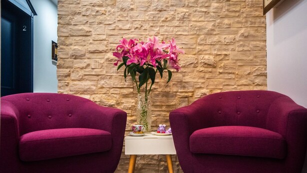 Two purple armchairs, a small white table, and a vase with pink flowers against a stone wall. - Center Luxury Rooms 3 (Split)