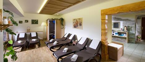 Une salle de spa dotée d’un plancher en bois, de fauteuils inclinables avec des serviettes, d’une table de massage, d’une lampe fixée au mur et offrant une vue sur un mur de pierre à travers une arche.