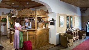 Ein Empfangsbereich mit einem Holzbüro, einem Mann und einer Frau sowie einem roten Koffer.