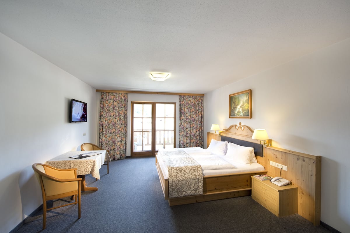 A hotel room with a bed, bedside table, desk, chair, and a television.