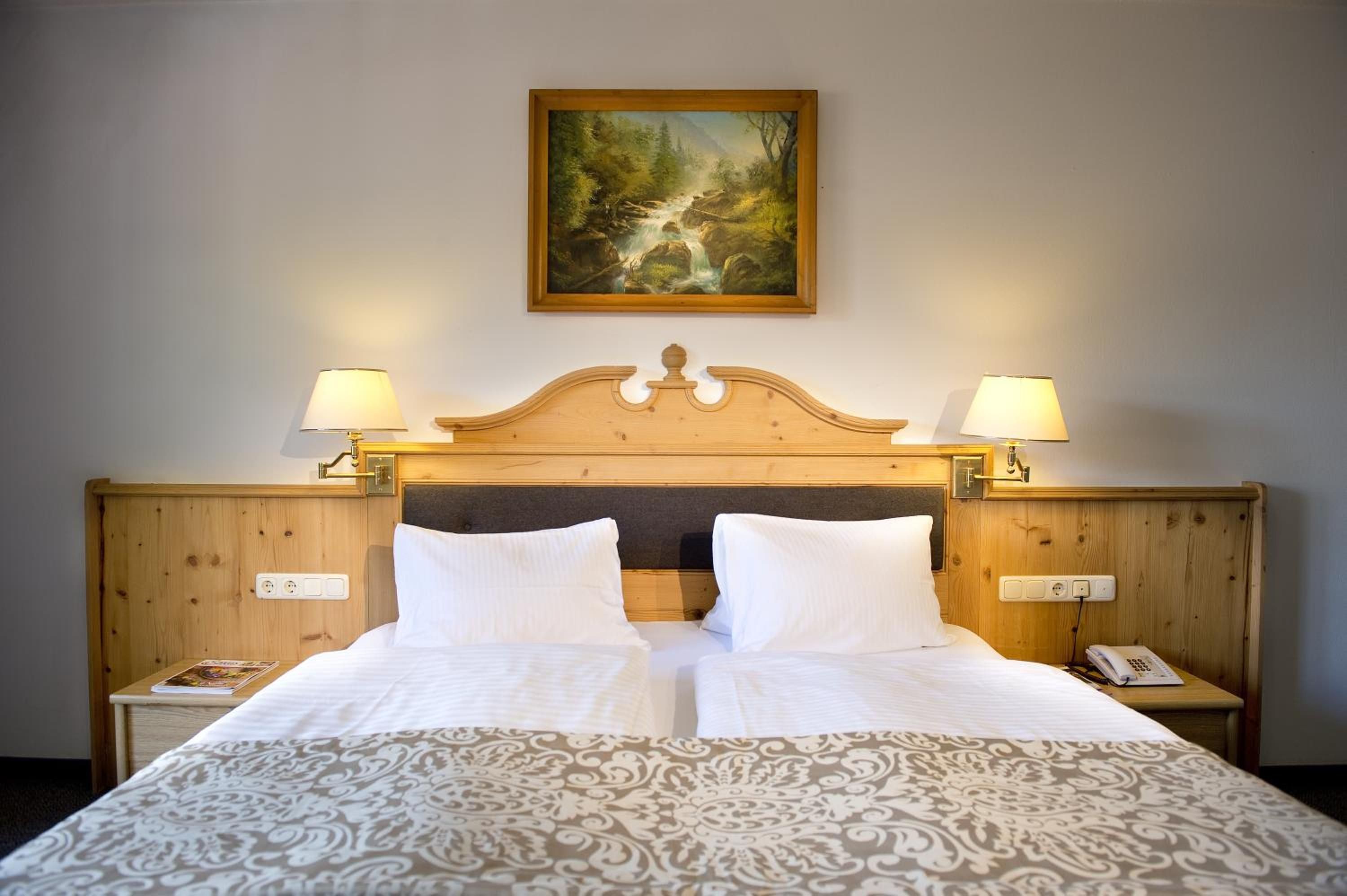 A hotel room with a large bed, two bedside lamps, a painting on the wall, and a wooden headboard.