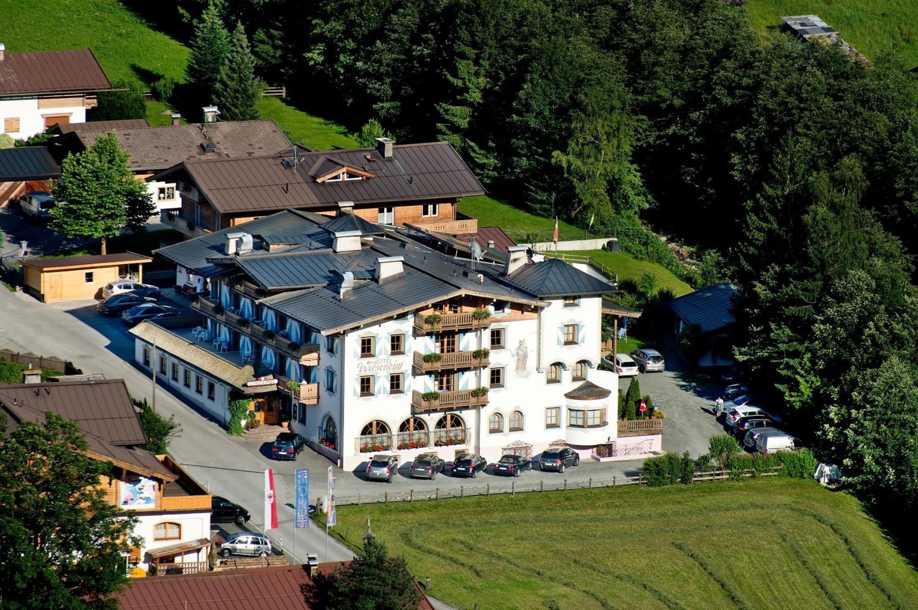 A multi-story hotel with a prominent balcony on the second floor, surrounded by lush greenery.