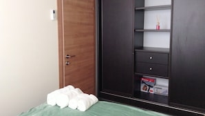 Un dormitori amb una porta de fusta, un armari amb calaixos i prestatges, un llit amb roba de llit verda, i una caixa d'assecador a la calaix inferior.