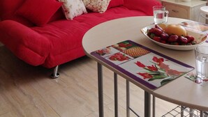 Un sofà vermell amb coixins florals, una taula petita amb un plat de fruita i un got d'aigua, i un aire condicionat fixat a la paret.